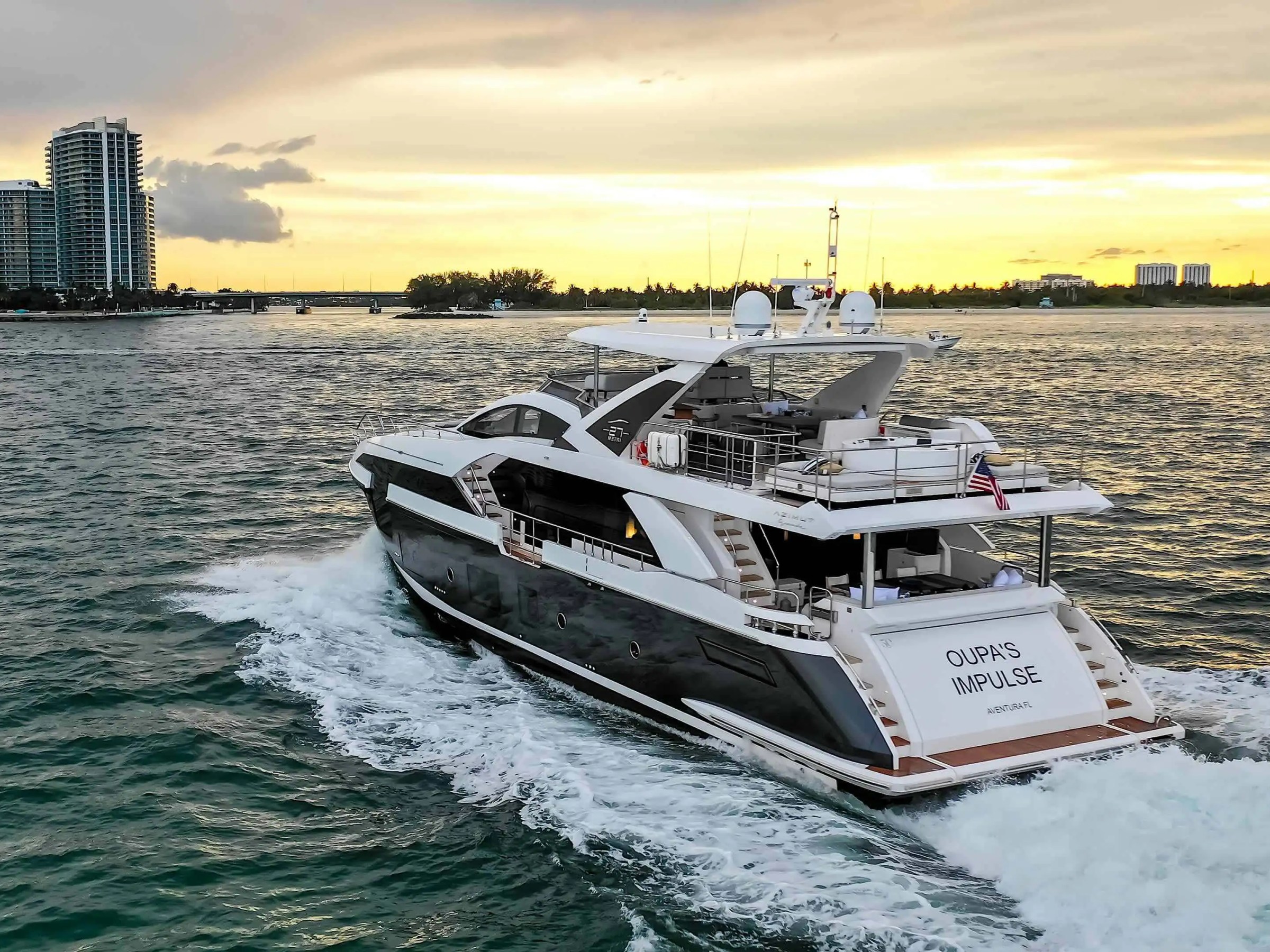 Aerial view of the 88 Azimut Yacht Charter cruising through Nassau Harbor at sunset, showcasing the expansive aft decks, flybridge, and luxury yacht design against the Bahamas skyline.