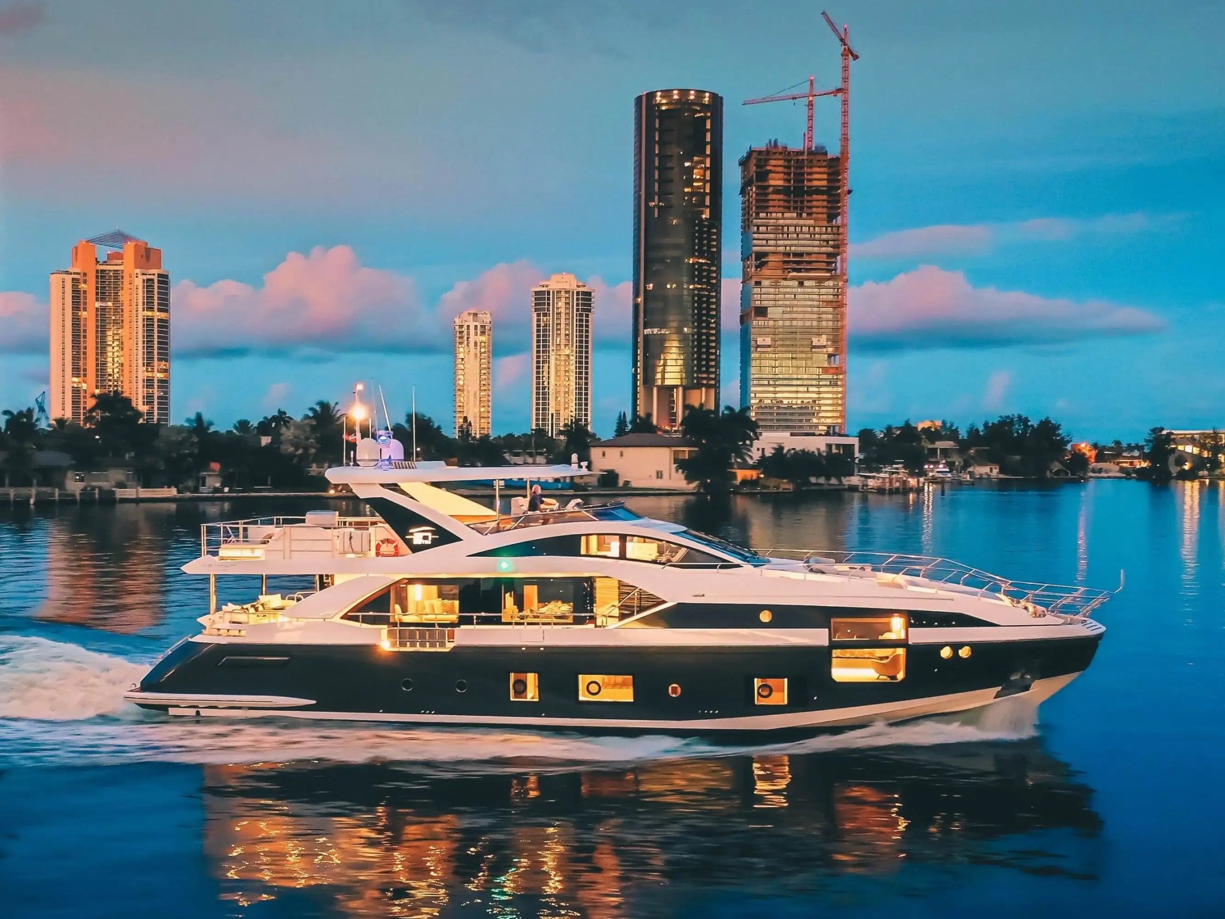 88 Azimut Yacht Charter cruising through Nassau Harbor at twilight with illuminated skyline reflections, luxury motor yacht underway near Bay Street Marina in The Bahamas