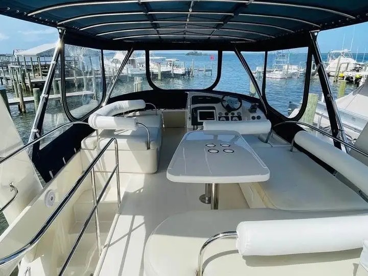 This 38 foot Aquila Boat Rental features the covered flybridge lounge with helm station, wraparound seating, and dining table dockside in Melbourne, Florida.
