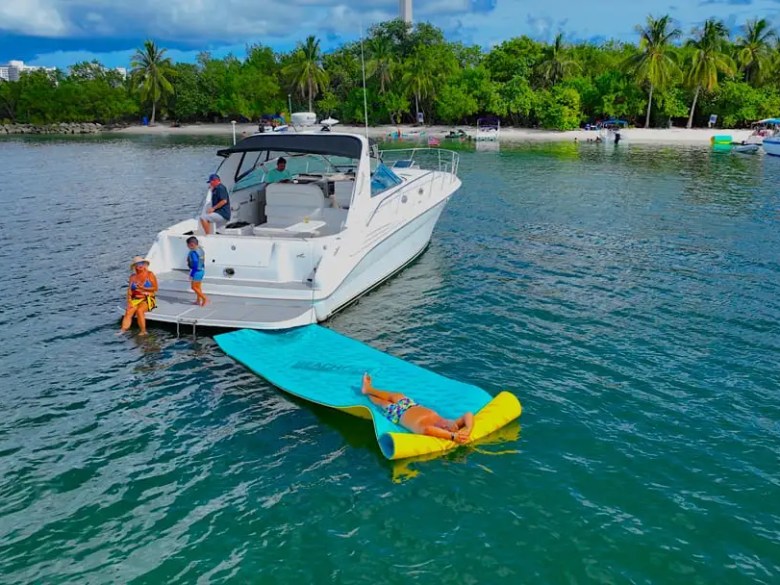 45 foot SeaRay Boat Rental captured in an aerial view off Hollywood, Florida with guests enjoying a floating water mat beside the swim platform near a tropical South Florida shoreline.