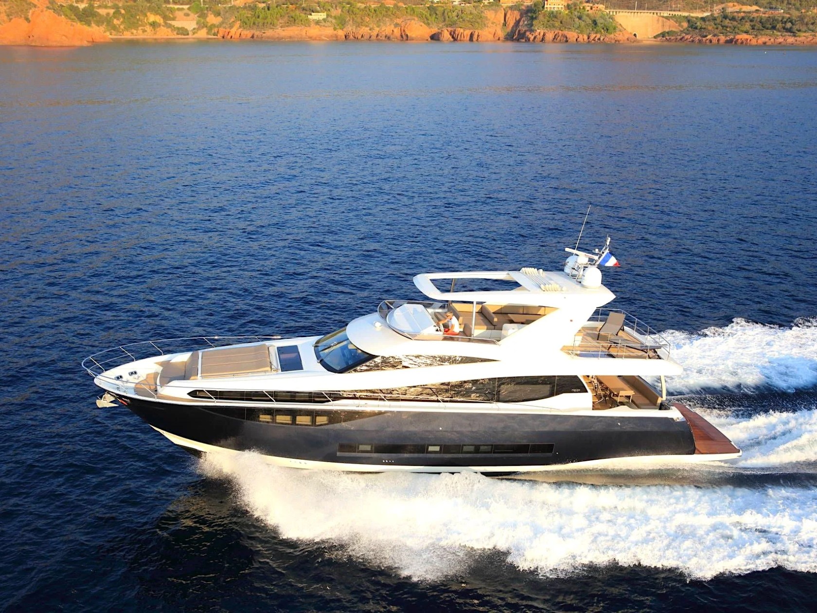 Luxury flybridge yacht cruising at speed across deep blue coastal waters with a spacious upper deck and panoramic ocean views.