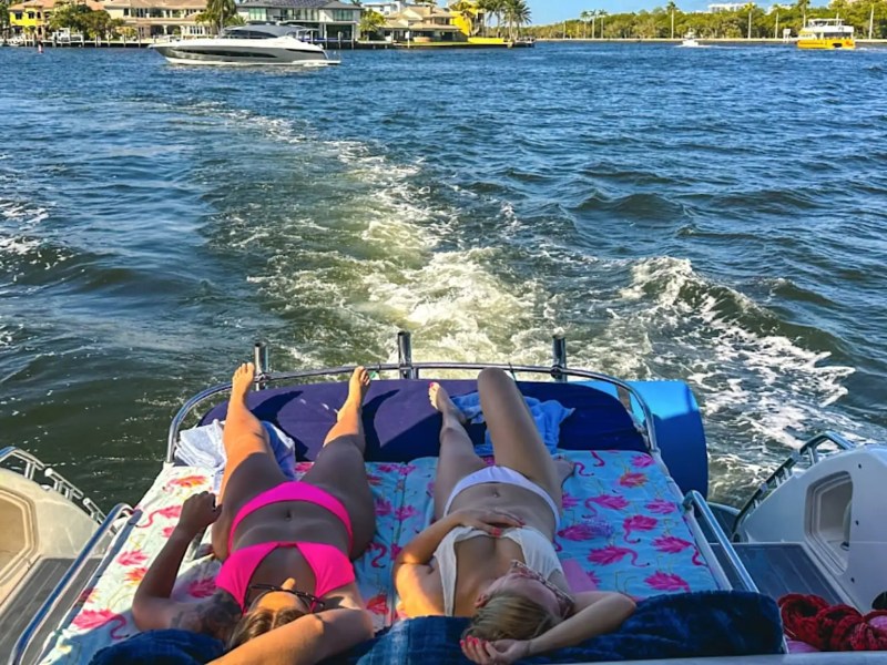 Guests relaxing on the aft sunpad of a 50′ Fairline yacht while cruising through Fort Lauderdale waterways with panoramic Intracoastal views.