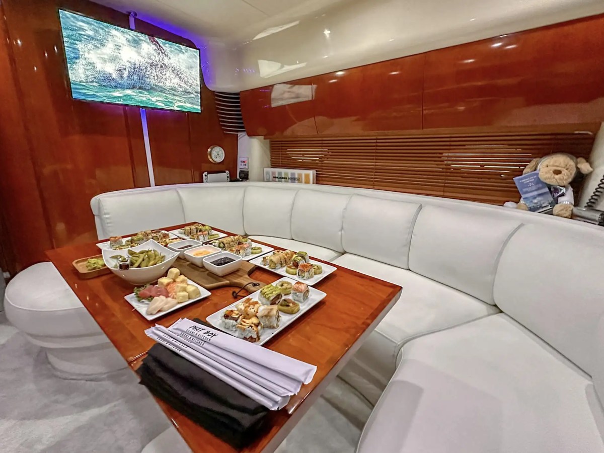 Interior dining lounge aboard a 50′ Fairline yacht featuring wraparound white seating, gourmet appetizers, polished wood table, and luxury cabin finishes in Fort Lauderdale.