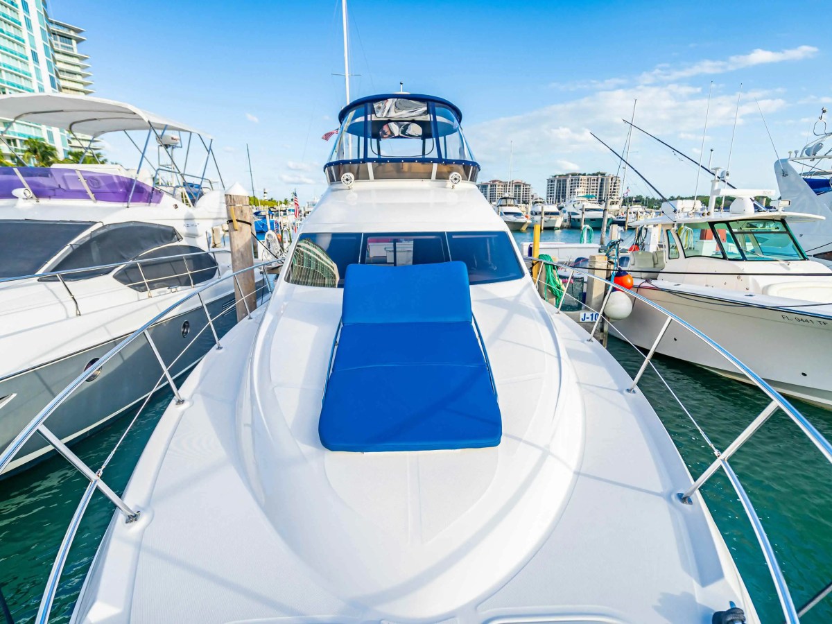 50' SeaRay [2] Yacht Charter bow sun pad featuring a blue lounge cushion, wide walkaround decks, enclosed flybridge, and Miami Beach marina views along Biscayne Bay