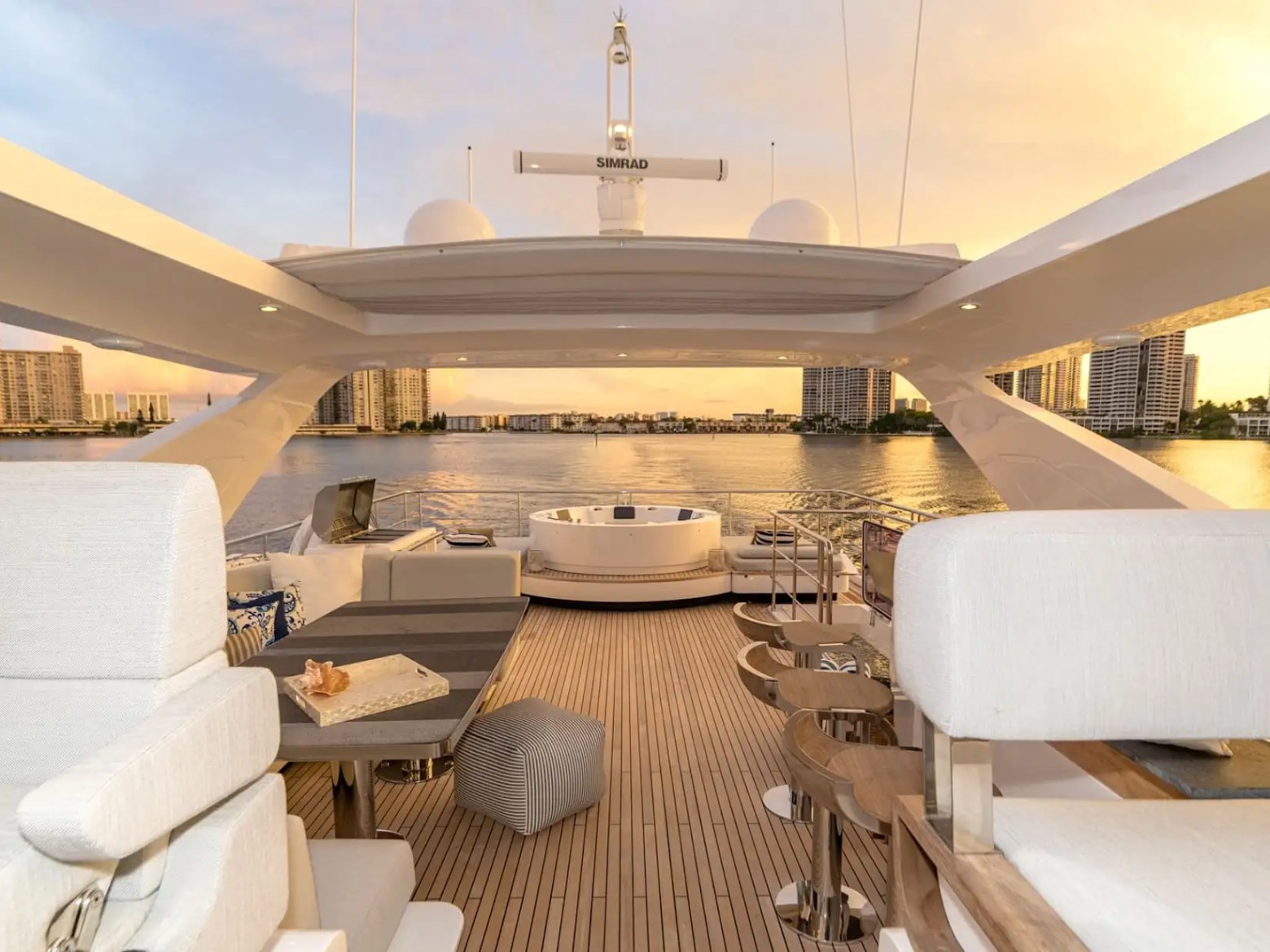 88 Azimut Yacht Charter flybridge lounge overlooking Nassau waterfront at sunset, featuring teak decking, outdoor seating, jacuzzi area, and skyline views