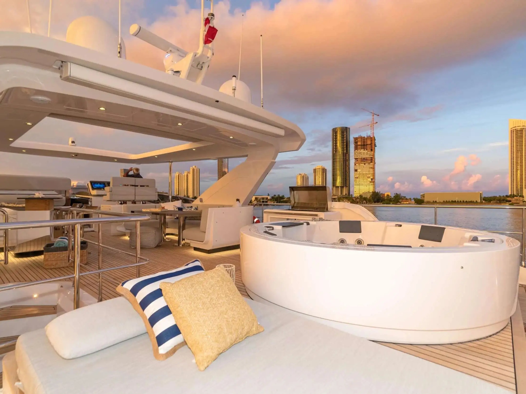 88 Azimut Yacht Charter sky deck featuring a waterfront jacuzzi, sun lounge seating, teak decking, and Nassau skyline views during a colorful Bahamas sunset