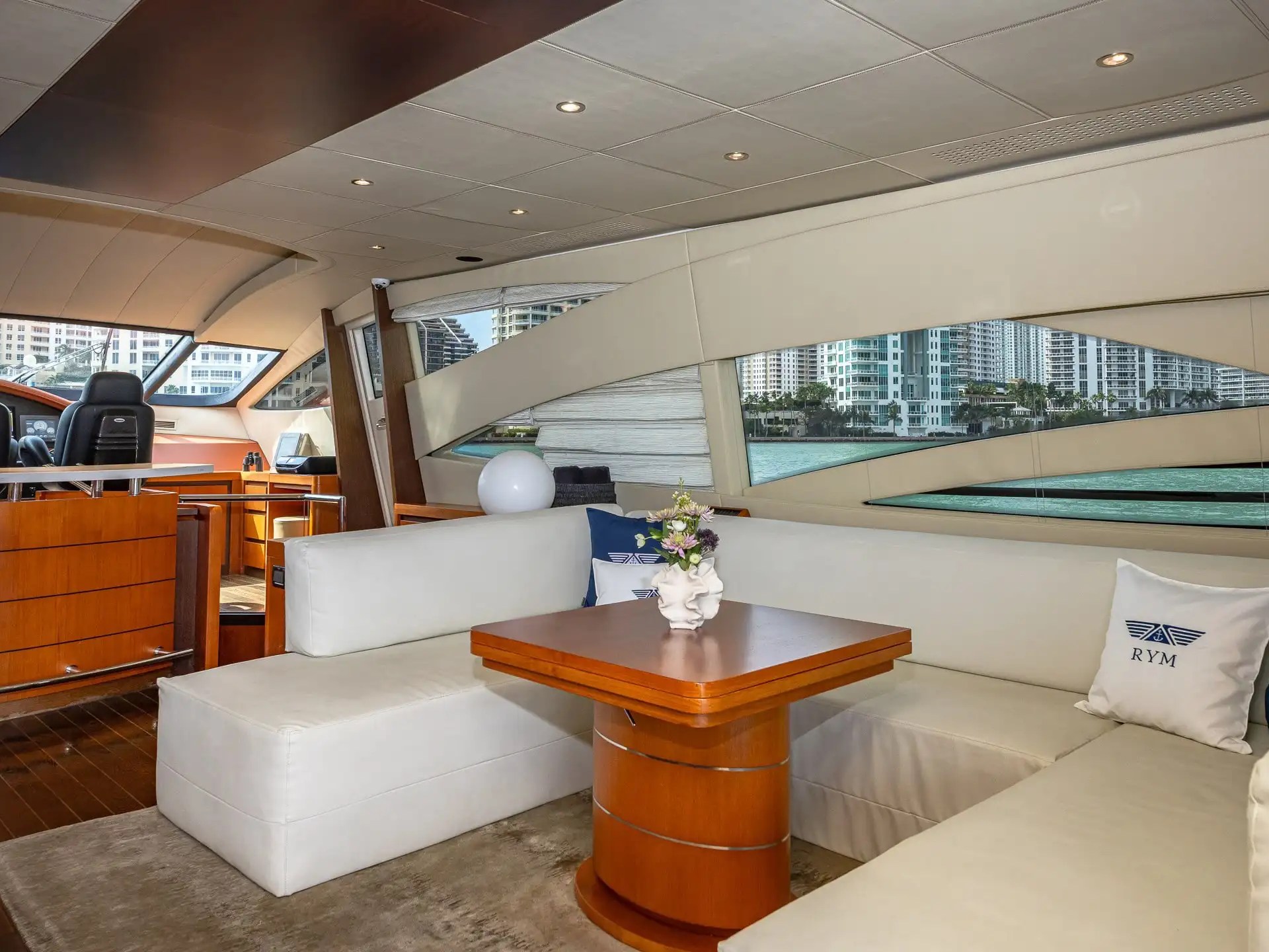 90 Pershing Yacht Charter salon lounge featuring wraparound seating, dining table, panoramic windows, and Brickell waterfront views during Miami cruising