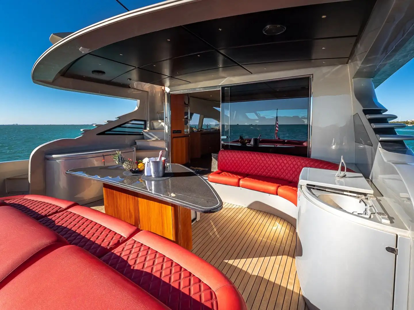 90 Pershing Yacht Charter aft entertainment deck featuring red diamond-stitched lounge seating, outdoor dining table, teak decking, and open South Florida cruising views