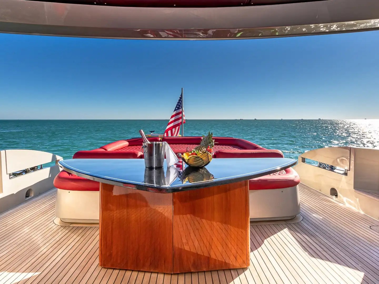 90 Pershing Yacht Charter aft deck lounge with red seating, dining table, ocean views, and Miami coastal scenery on South Florida waters