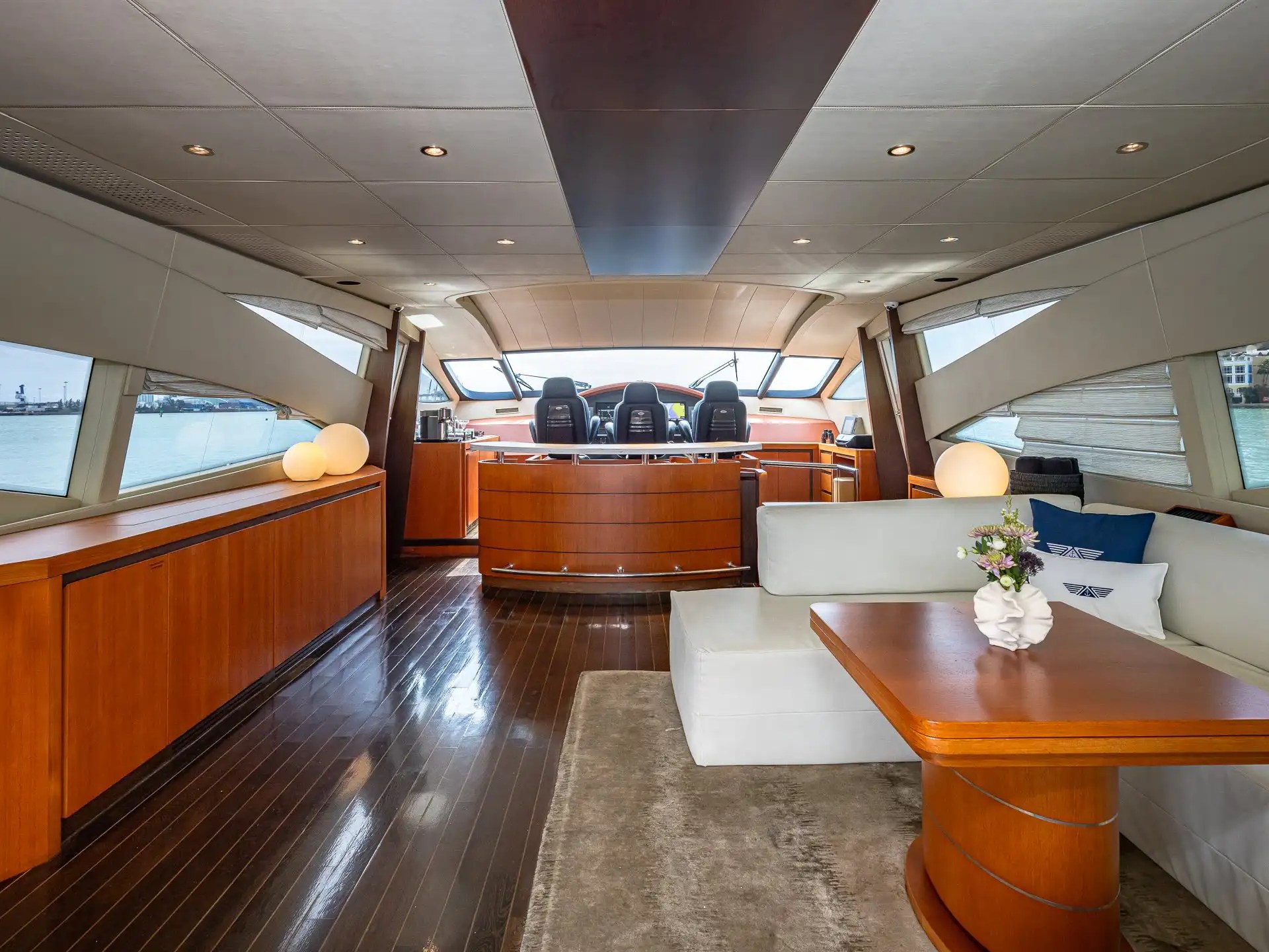 90 Pershing Yacht Charter salon interior featuring wraparound seating, wood flooring, dining table, panoramic windows, and Miami waterfront views