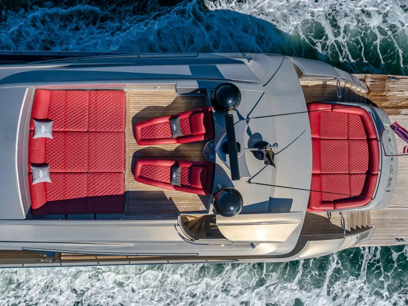 90 Pershing Yacht Charter drone shot showcasing red sun pads, teak decking, and aft lounge seating while cruising through Miami coastal waters
