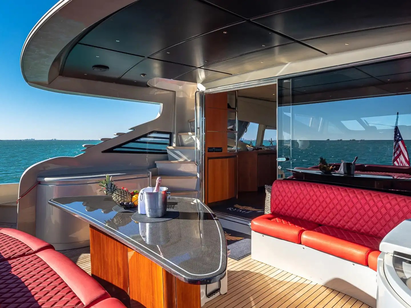 90 Pershing Yacht Charter aft deck featuring red lounge seating, outdoor dining table, teak decking, and open Miami ocean views in South Florida