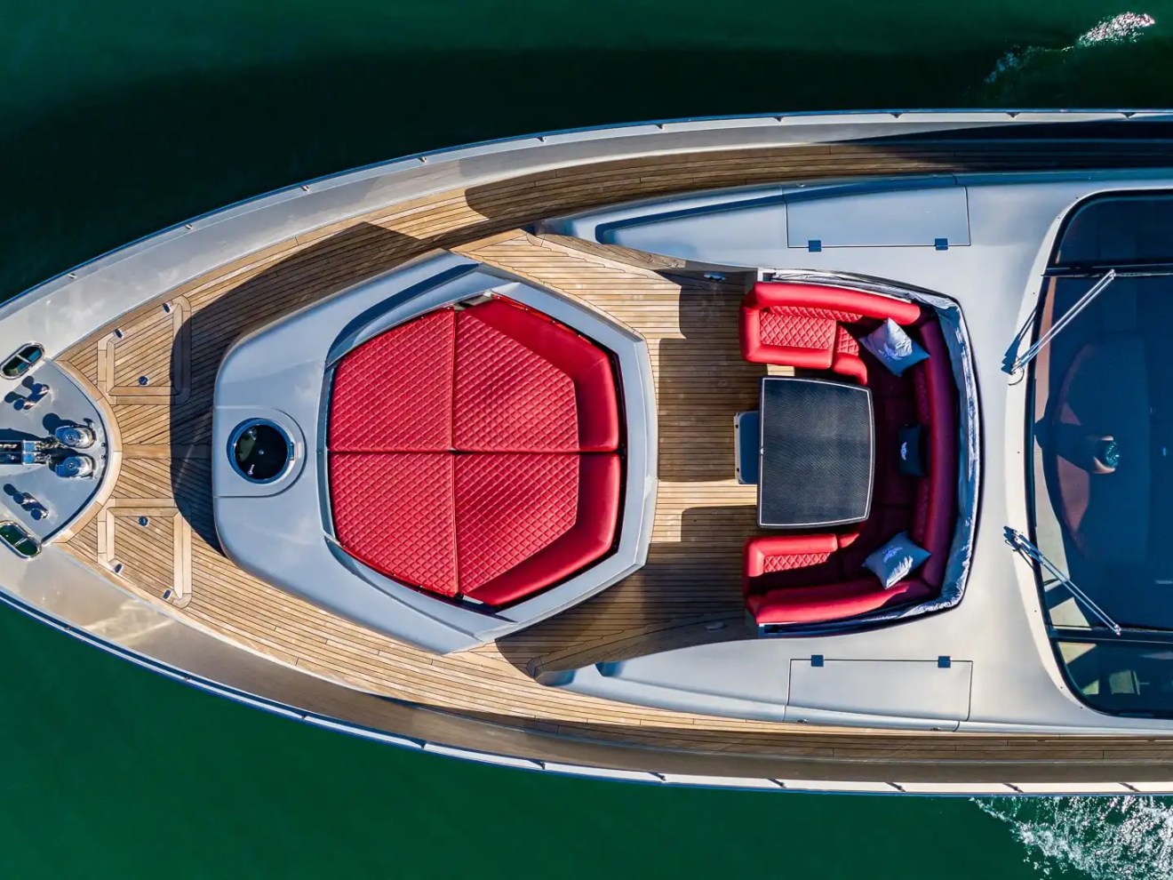 90 Pershing Yacht Charter drone shot of bow lounge featuring red sun pad, forward seating area, teak decking, and Miami coastal waters below
