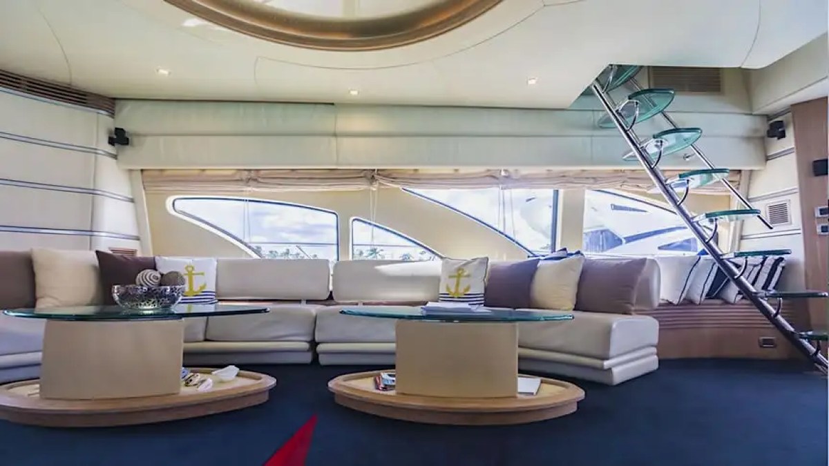 Modern yacht interior with curved sofa, glass tables, and a spiral staircase.