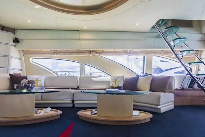 Modern yacht interior with curved sofa, glass tables, and a spiral staircase.
