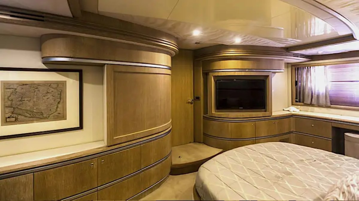 Luxurious yacht cabin with wood paneling, wall art, and a bed; features a TV and window with blinds.