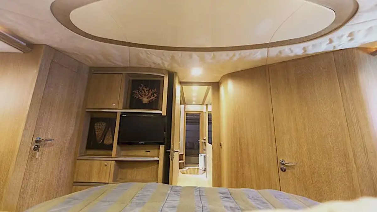 Cozy yacht cabin with wood panels, bed, TV, and decorative items on shelves.