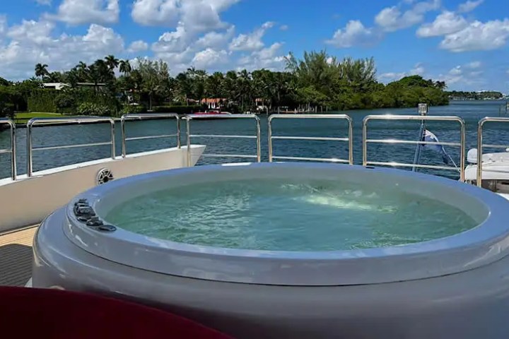 Hot tub on a yacht deck with scenic view of water, trees, and sky.
