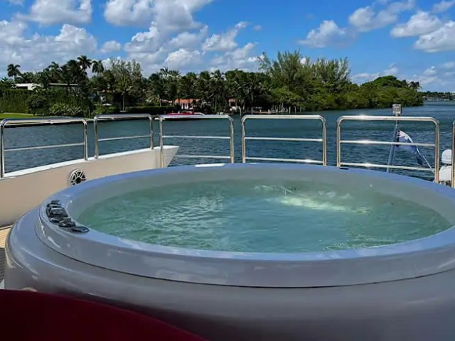 Hot tub on a yacht deck with scenic view of water, trees, and sky.