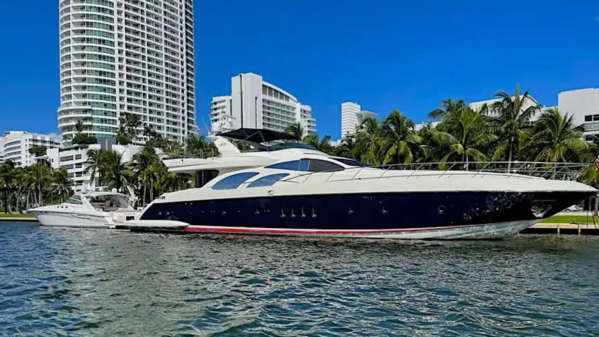 Luxury yacht docked near palm trees and tall buildings on a clear day.