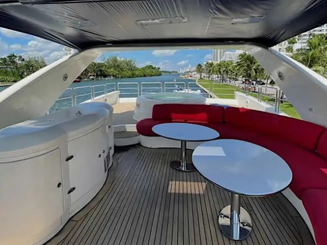 Luxury yacht deck with red seating, tables, and view of water and buildings.