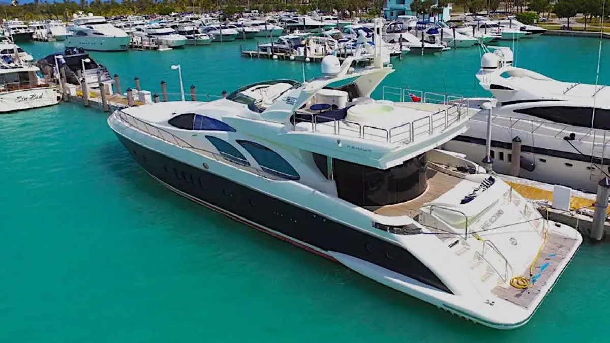 A large yacht docked in a marina with turquoise water and multiple boats in the background.