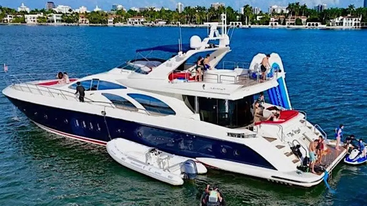 Luxury yacht in the water with people enjoying slide and jet skis nearby.