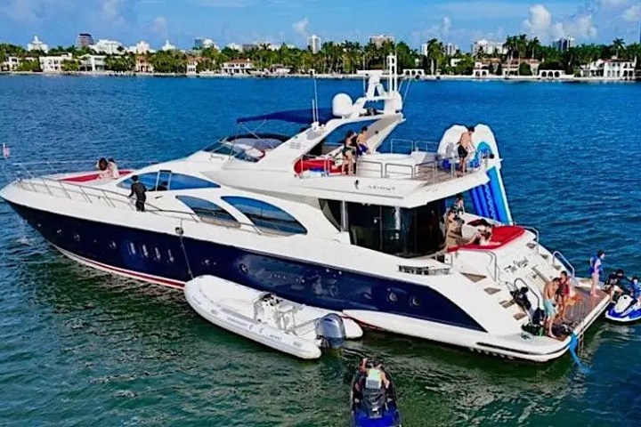 Luxury yacht in the water with people enjoying slide and jet skis nearby.