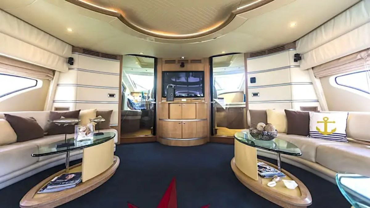 Spacious yacht interior with beige seating, glass tables, and a TV, featuring nautical decor.