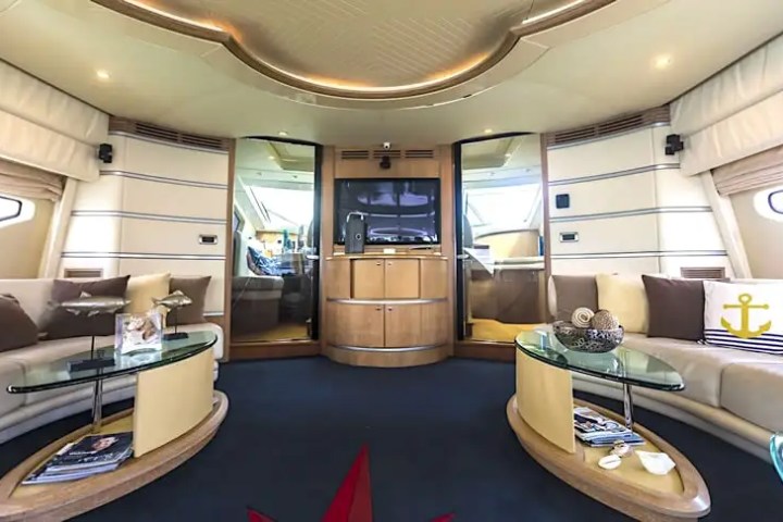 Spacious yacht interior with beige seating, glass tables, and a TV, featuring nautical decor.