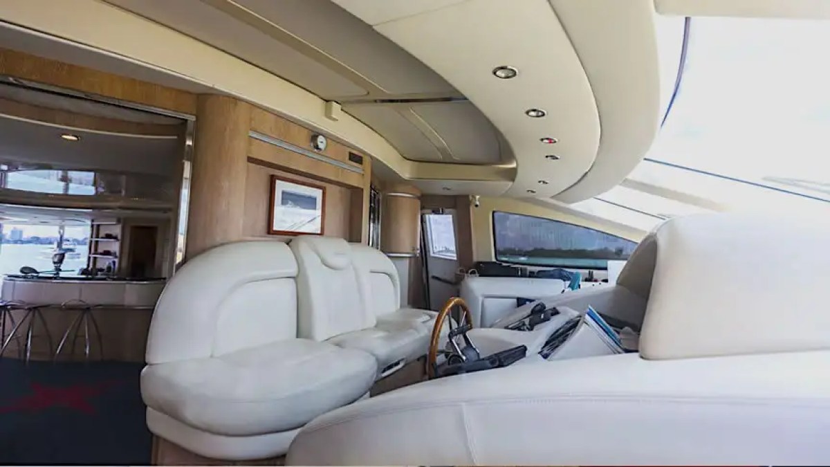 Luxurious yacht interior with white leather seating and modern controls, overlooking water through large windows.