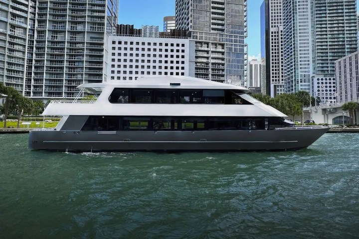 A modern yacht on water with city skyscrapers in the background.