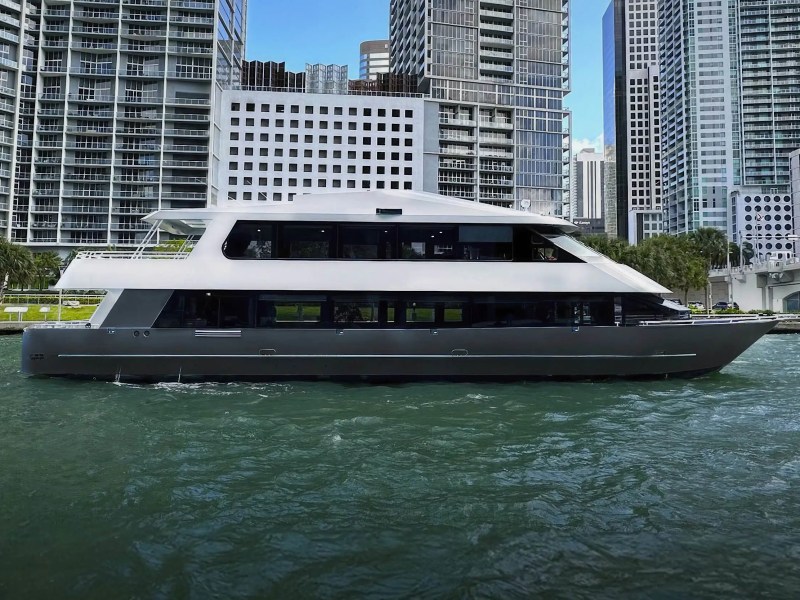 A modern yacht on water with city skyscrapers in the background.