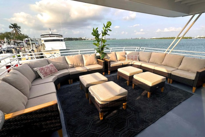 Outdoor seating area with beige cushions on a yacht with a view of water and a docked boat.