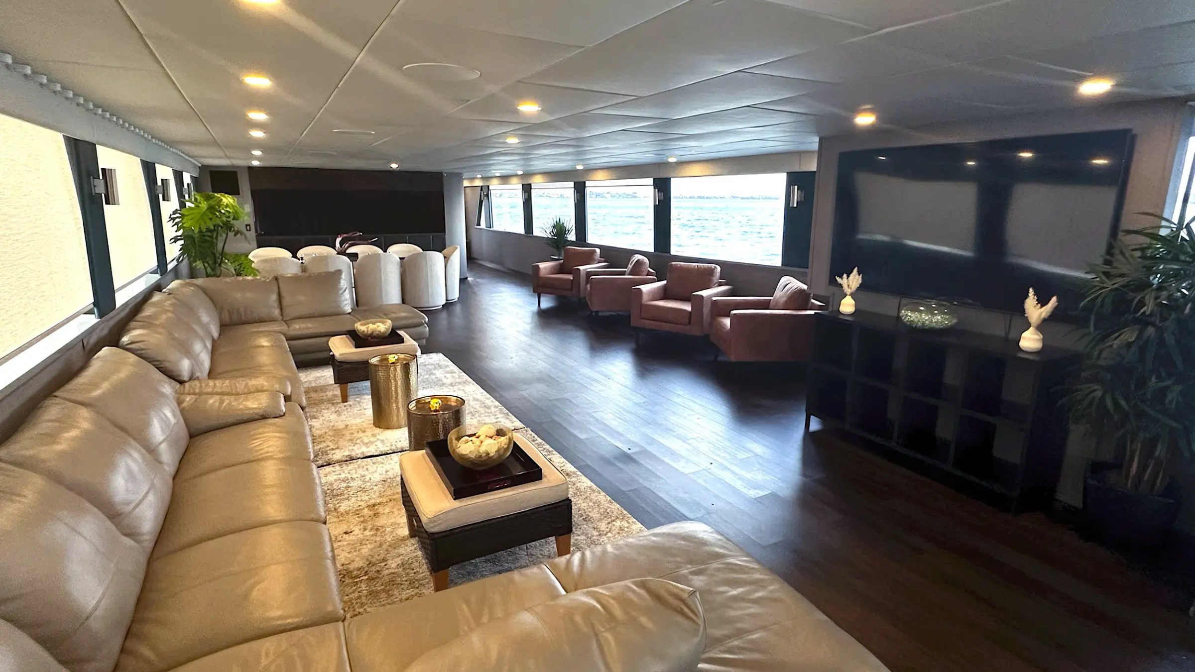 Spacious lounge with leather sofas, armchairs, decorative items, and large windows overlooking the water.