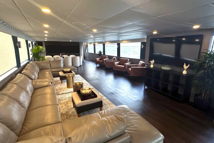 Spacious lounge with leather sofas, armchairs, decorative items, and large windows overlooking the water.