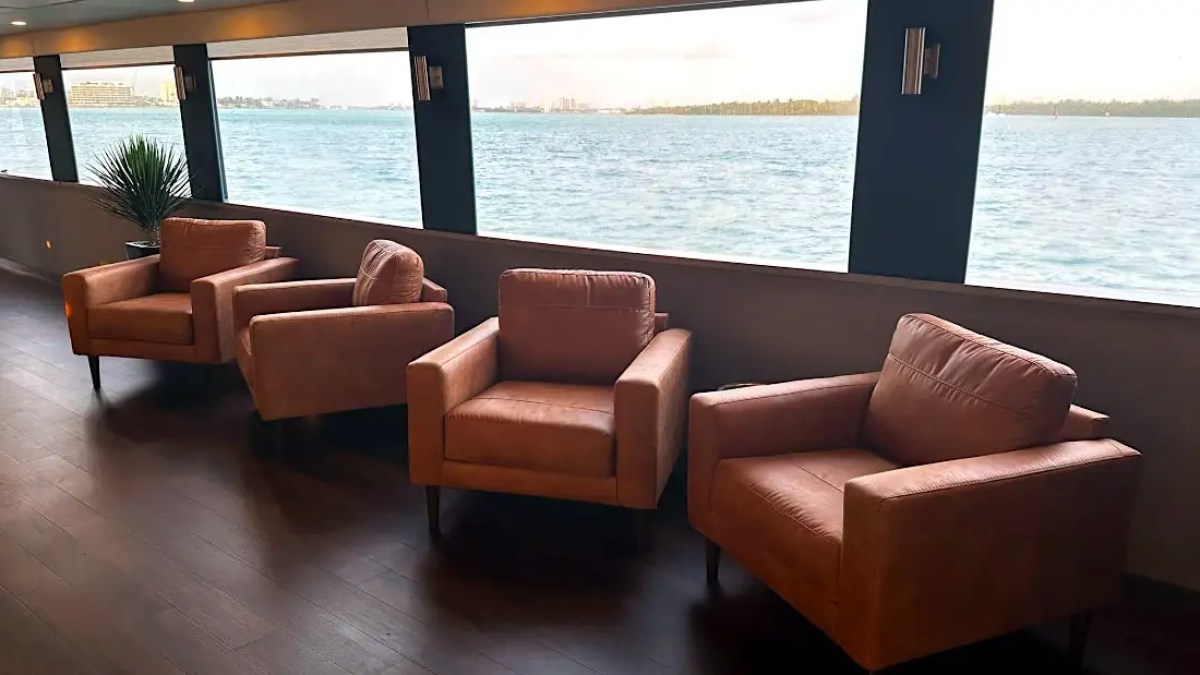 Three brown armchairs facing large windows with ocean view on a ship.