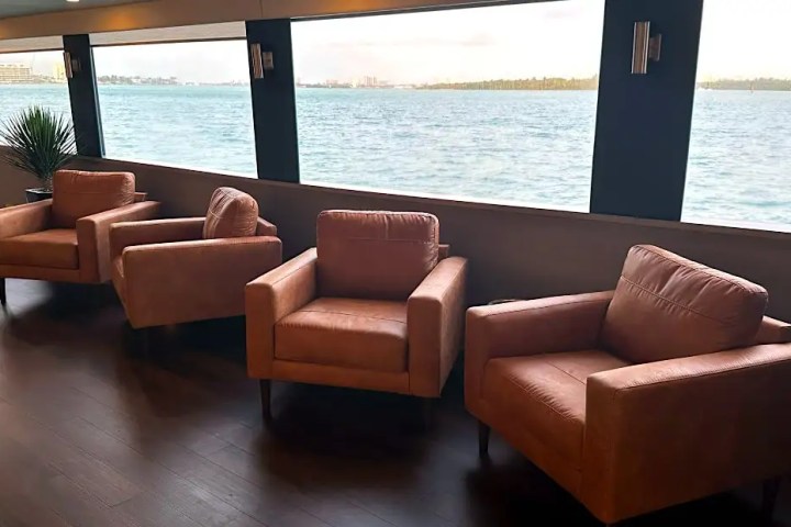 Three brown armchairs facing large windows with ocean view on a ship.
