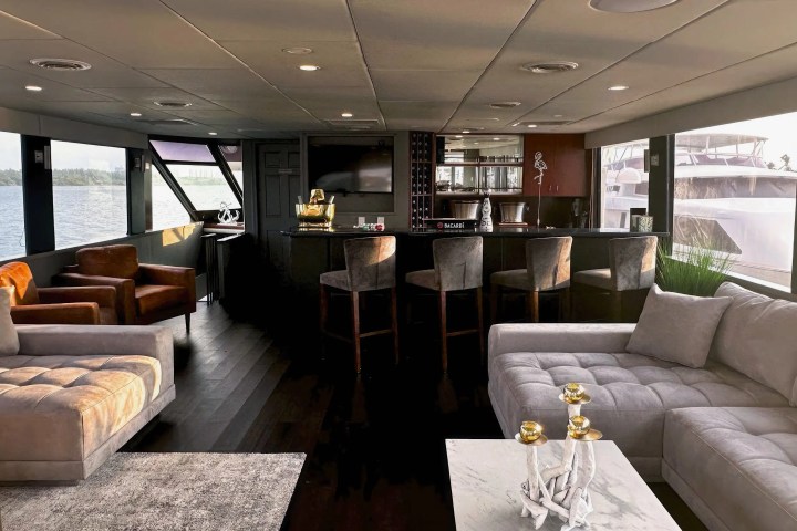 Luxurious yacht interior with sofas, armchairs, a bar, and panoramic windows overlooking the water.