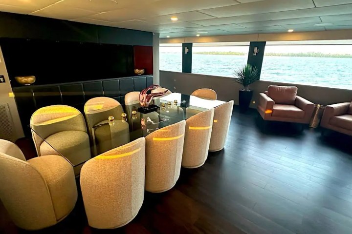 Luxurious yacht interior with dining table, chairs, armchairs, and sea view through large windows.
