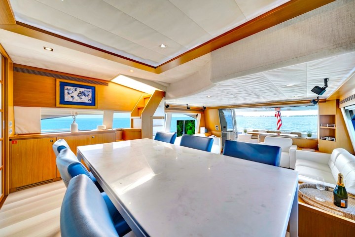 Luxurious yacht interior with marble table, blue chairs, and ocean view through wide windows.
