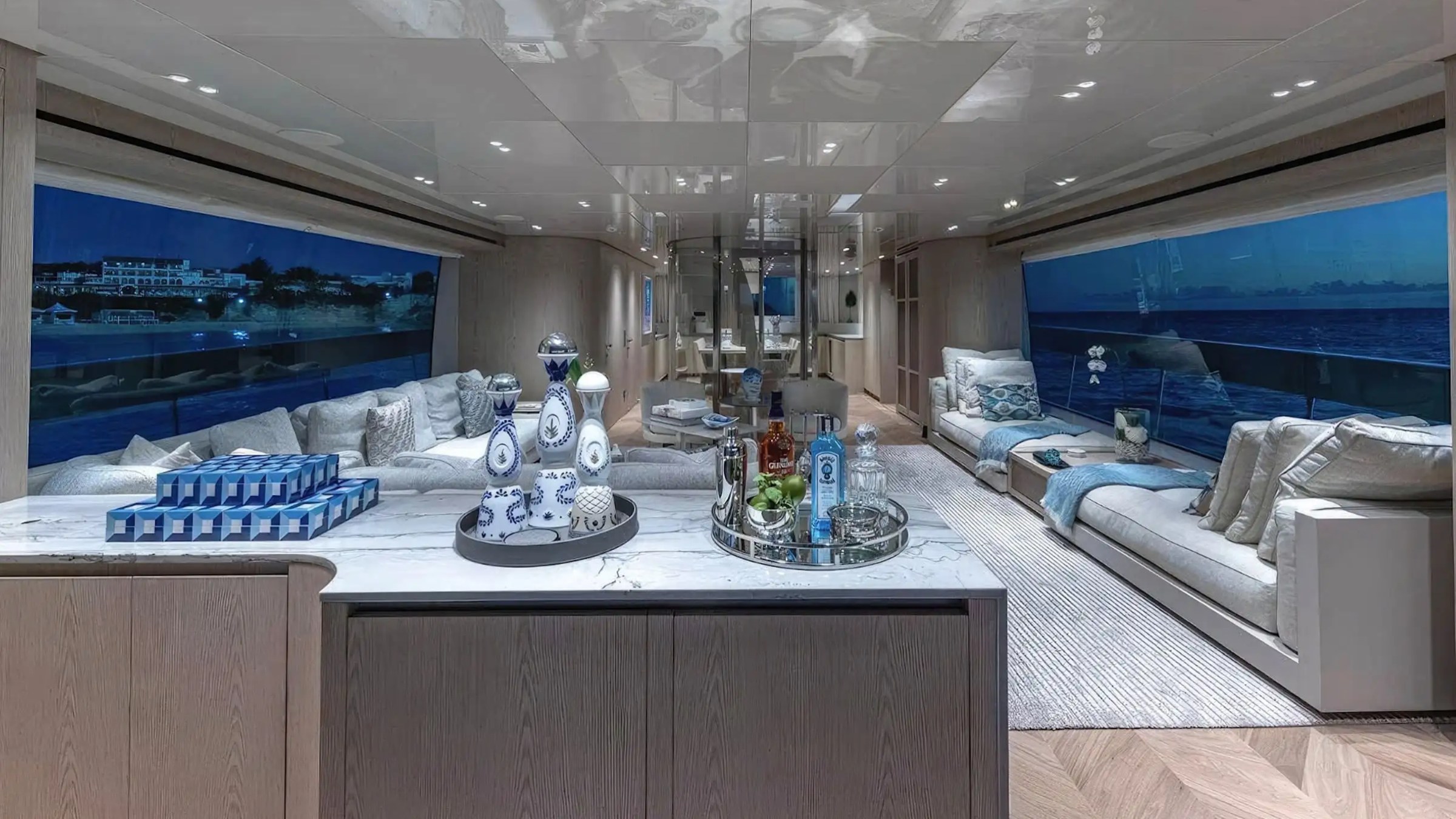 Luxurious yacht interior with marble counter and large windows, set for drinks and snacks at sunset.