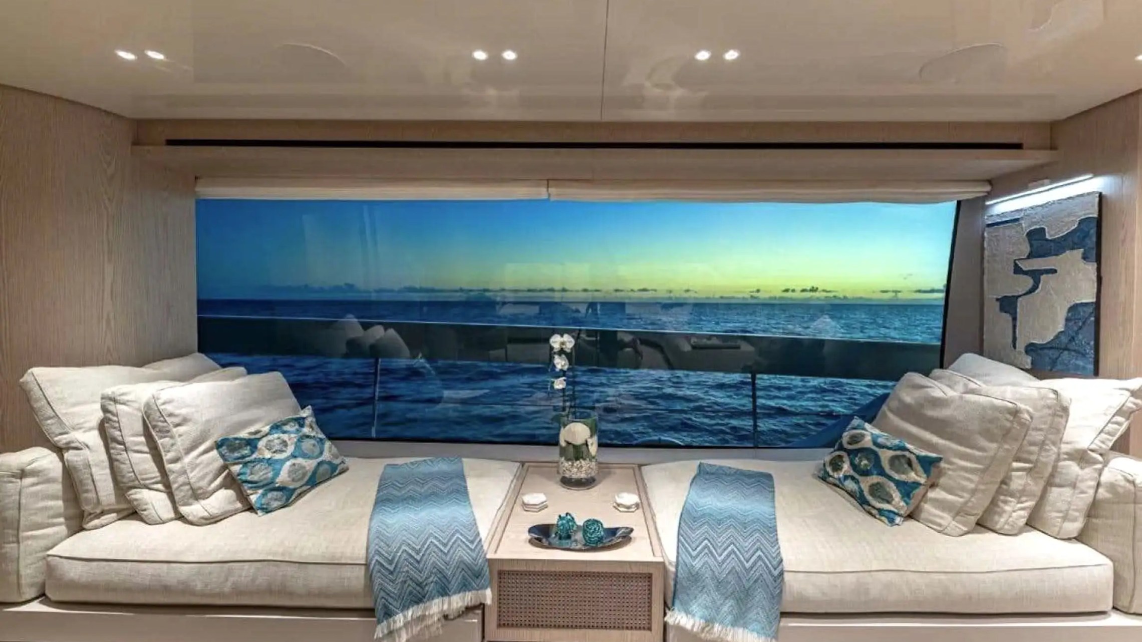 Luxury yacht interior with ocean view, two sofas, cushions, and a coffee table with decor.