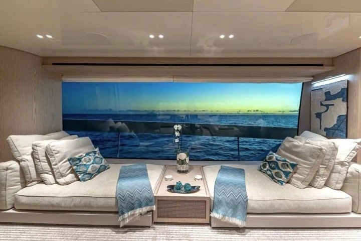 Luxury yacht interior with ocean view, two sofas, cushions, and a coffee table with decor.