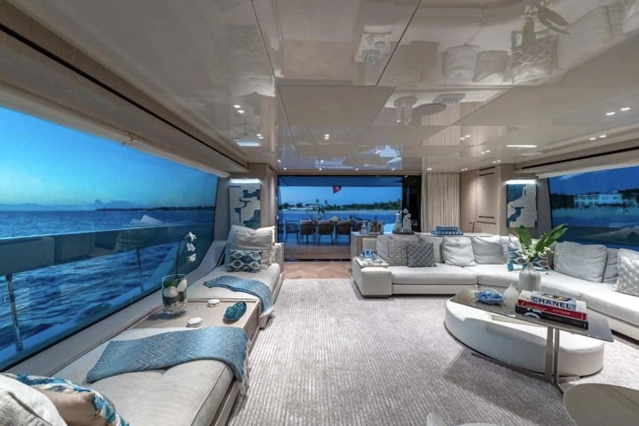 Luxurious yacht interior with white sofas, blue accents, large windows, and ocean view.