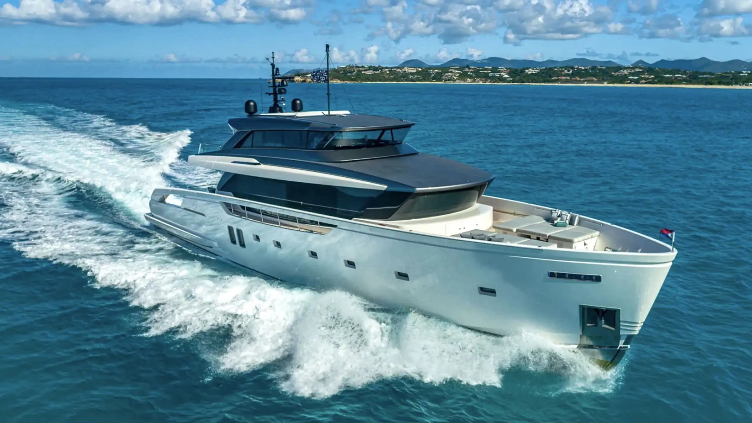 Modern yacht cruising on blue ocean near distant coastline under cloudy sky.