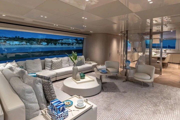 Luxurious yacht interior with spacious seating, large window view of coast, and modern decor.