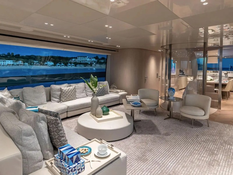 Luxurious yacht interior with spacious seating, large window view of coast, and modern decor.