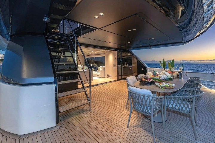 Luxurious yacht deck with dining table, staircase, and ocean view at sunset.