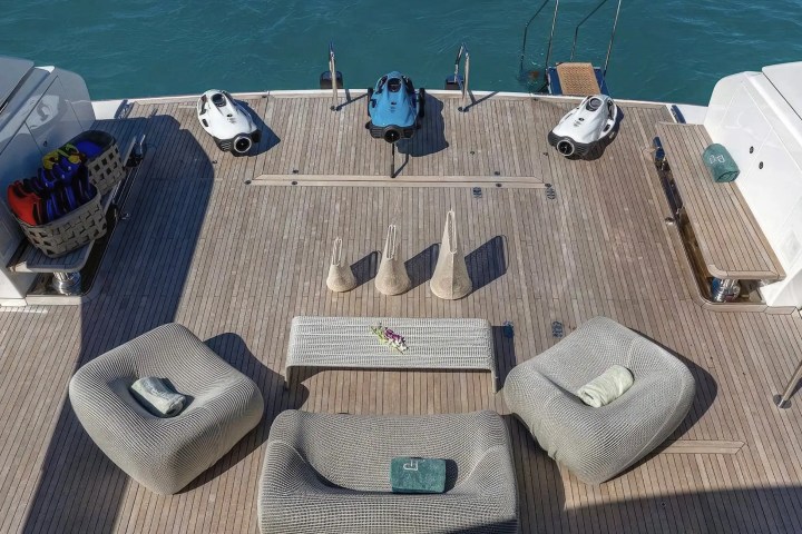 Yacht deck with seating, table, diving gear, and three underwater scooters; view of water in the background.